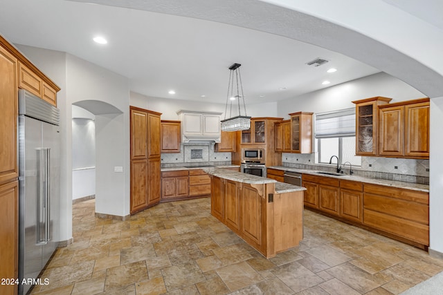 kitchen featuring a center island, built in appliances, sink, tasteful backsplash, and decorative light fixtures