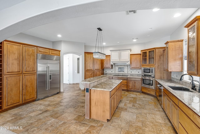 kitchen with built in appliances, decorative backsplash, hanging light fixtures, sink, and a kitchen island