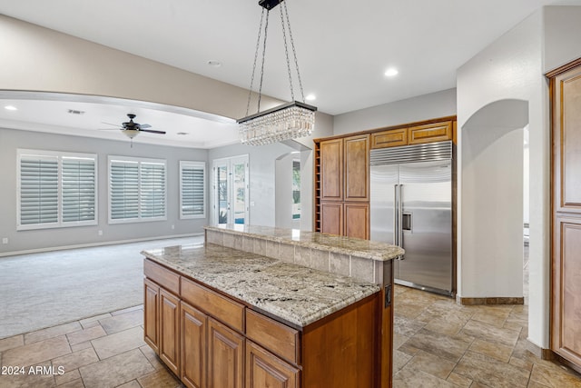 kitchen featuring light stone countertops, stainless steel built in fridge, a center island, light colored carpet, and pendant lighting