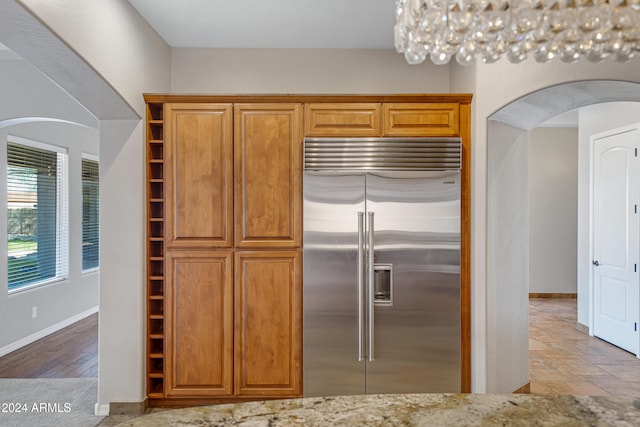 kitchen featuring stainless steel built in fridge, light hardwood / wood-style floors, and light stone counters