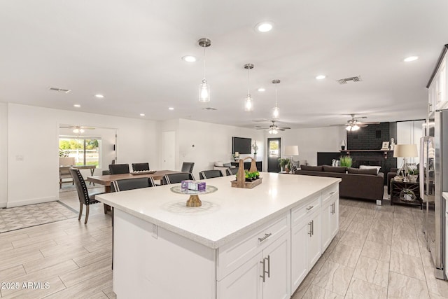 kitchen featuring decorative light fixtures, stainless steel refrigerator, white cabinets, and a kitchen island