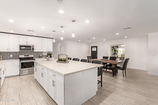 kitchen featuring a kitchen bar, a center island, hanging light fixtures, stainless steel appliances, and white cabinets