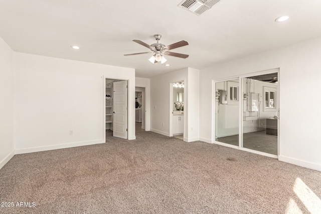 unfurnished bedroom with ensuite bathroom, a walk in closet, carpet flooring, a closet, and ceiling fan