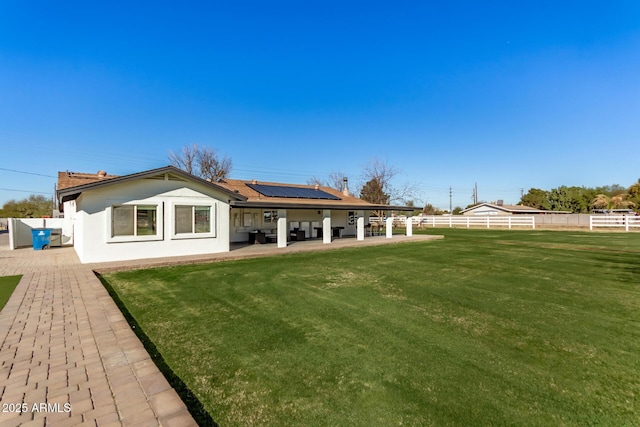 rear view of property featuring a lawn, a patio, and solar panels