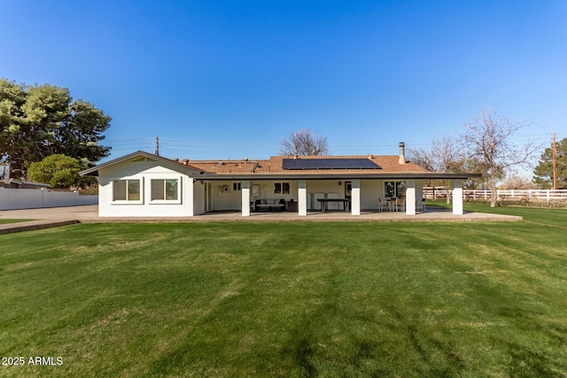 back of house featuring a yard, a patio area, and solar panels