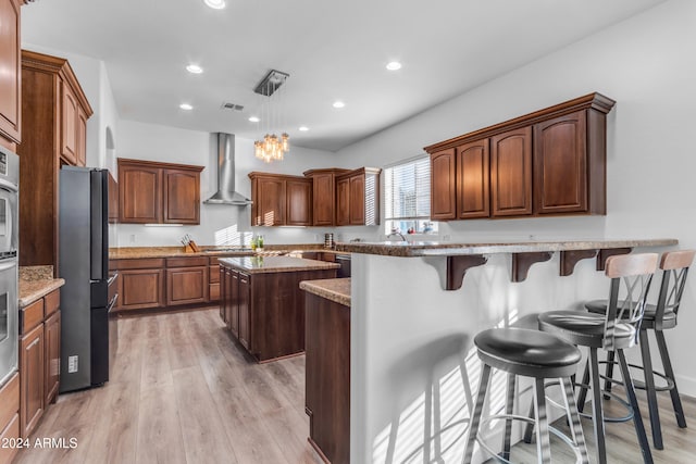 kitchen featuring wall chimney exhaust hood, a breakfast bar, a center island, appliances with stainless steel finishes, and pendant lighting