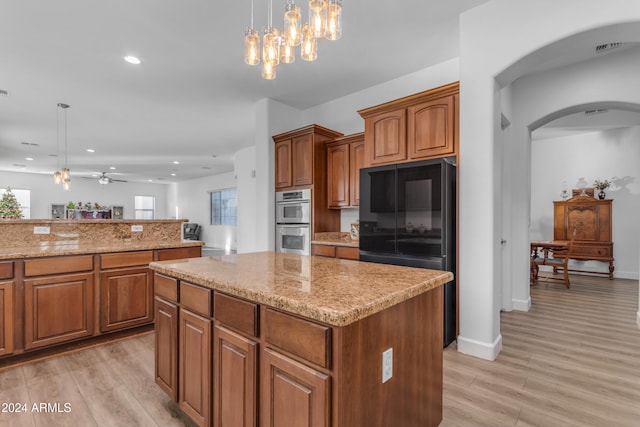 kitchen featuring a center island, light wood-type flooring, black refrigerator, pendant lighting, and stainless steel double oven