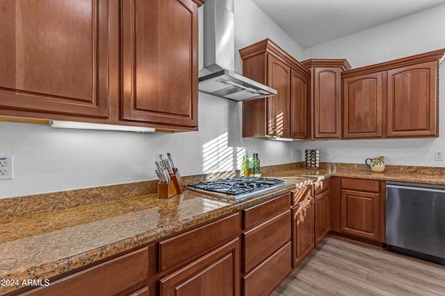 kitchen with stainless steel appliances, dark stone counters, light hardwood / wood-style floors, and wall chimney exhaust hood