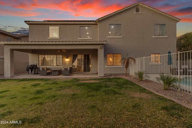 back house at dusk featuring an outdoor living space, a lawn, a patio, and ceiling fan