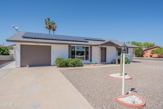 ranch-style home with an attached garage, solar panels, and concrete driveway