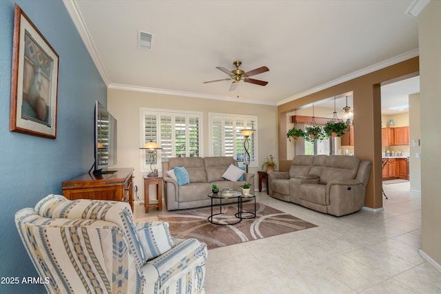 living area with light tile patterned floors, ceiling fan, visible vents, baseboards, and crown molding