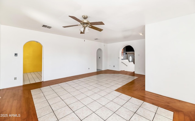 unfurnished room with a ceiling fan, arched walkways, visible vents, and parquet floors