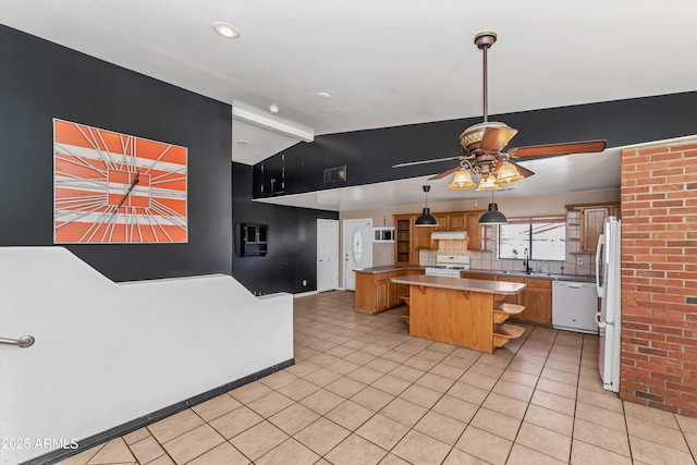 kitchen featuring white appliances, a sink, a kitchen island, light countertops, and brown cabinets