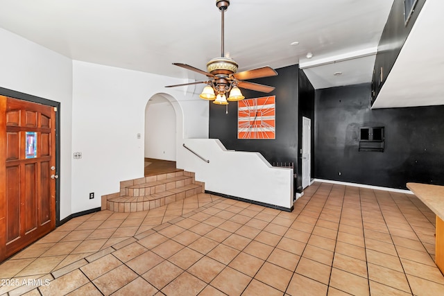 foyer featuring arched walkways, light tile patterned flooring, a ceiling fan, and baseboards