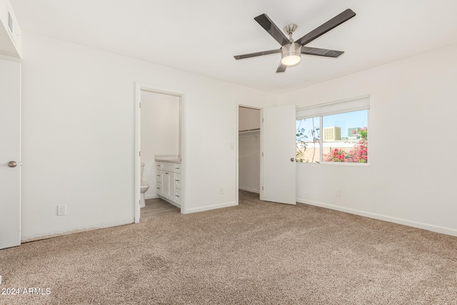 unfurnished bedroom featuring a spacious closet, ceiling fan, light carpet, and ensuite bath