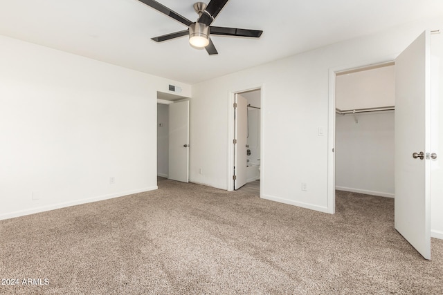 unfurnished bedroom with connected bathroom, a closet, a walk in closet, carpet, and ceiling fan