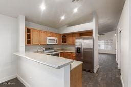 kitchen with kitchen peninsula, lofted ceiling, dark wood-type flooring, and stainless steel appliances