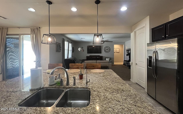 kitchen with light stone counters, stainless steel fridge with ice dispenser, open floor plan, and a sink