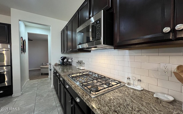 kitchen featuring light tile patterned floors, dark stone counters, stainless steel appliances, decorative backsplash, and dark cabinets