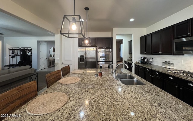 kitchen with a sink, light stone counters, decorative light fixtures, stainless steel appliances, and decorative backsplash