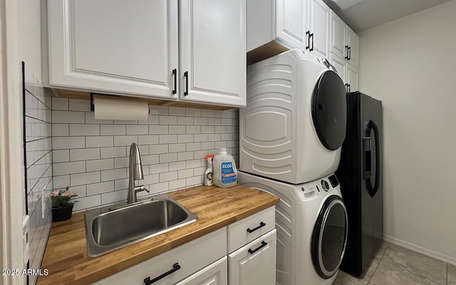 laundry room with baseboards, light tile patterned flooring, cabinet space, a sink, and stacked washer and dryer