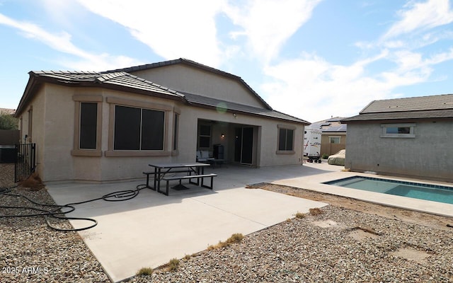 rear view of house with fence, a tile roof, stucco siding, a patio area, and an outdoor pool