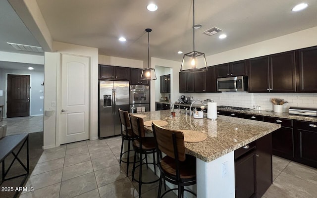 kitchen featuring visible vents, a breakfast bar, light stone counters, stainless steel appliances, and decorative backsplash