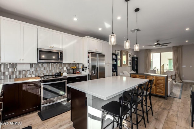 kitchen with white cabinets, open floor plan, decorative light fixtures, stainless steel appliances, and light countertops