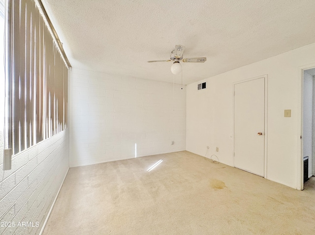 spare room featuring ceiling fan, brick wall, light colored carpet, and a textured ceiling