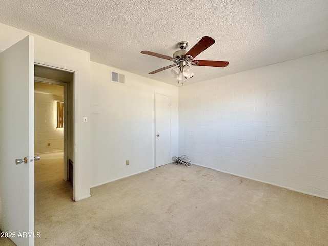 carpeted empty room with ceiling fan, a textured ceiling, and brick wall