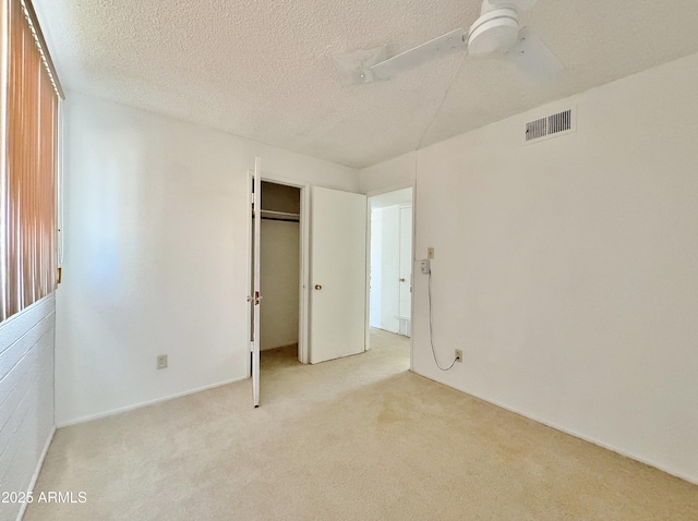 unfurnished bedroom with light carpet, a textured ceiling, a closet, and ceiling fan