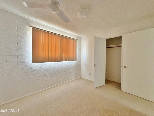 unfurnished bedroom with light carpet, a textured ceiling, a closet, ceiling fan, and brick wall