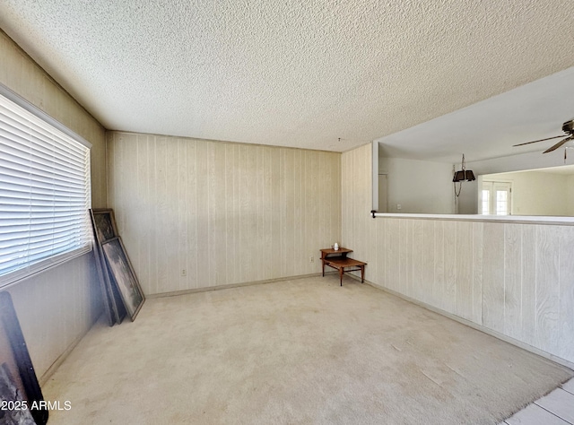 empty room with ceiling fan, a textured ceiling, and wood walls