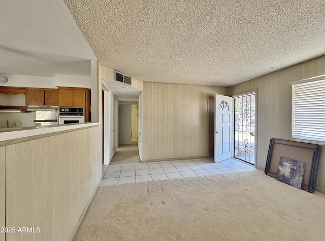 unfurnished living room with light colored carpet, wooden walls, and a textured ceiling