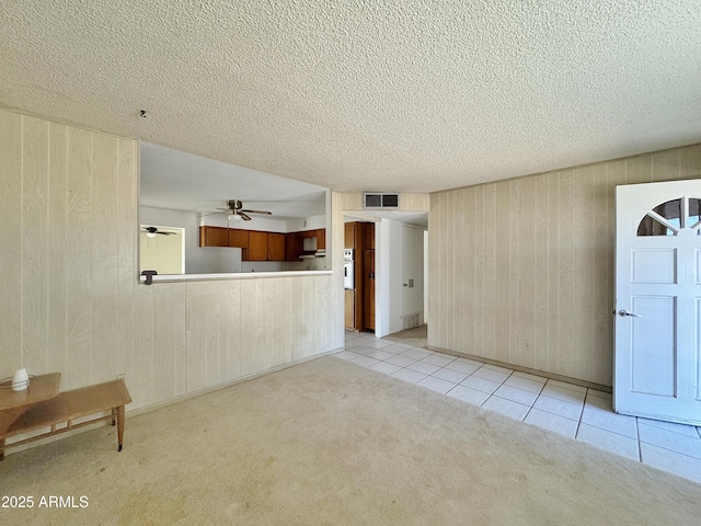 unfurnished living room featuring ceiling fan, wooden walls, and light tile patterned floors