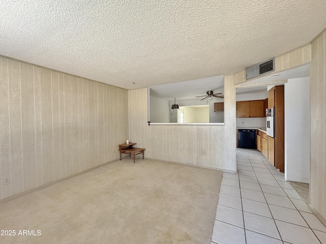 unfurnished living room featuring ceiling fan, light tile patterned floors, a textured ceiling, and wood walls