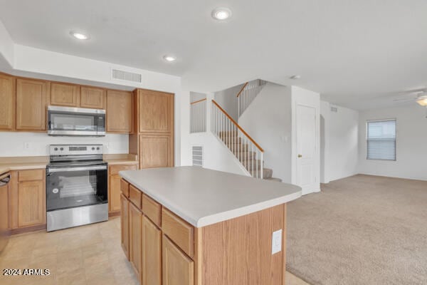 kitchen with appliances with stainless steel finishes, light carpet, ceiling fan, and a kitchen island