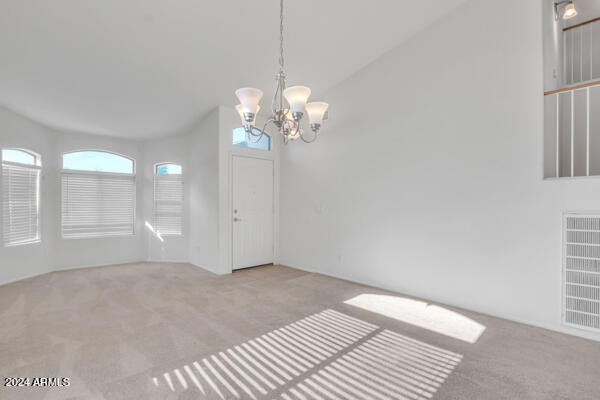 carpeted empty room featuring vaulted ceiling and a chandelier