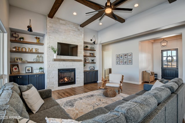 living room with a stone fireplace, wood finished floors, beam ceiling, and built in features