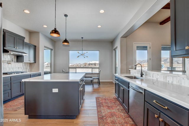 kitchen featuring light wood-style floors, appliances with stainless steel finishes, a sink, under cabinet range hood, and backsplash