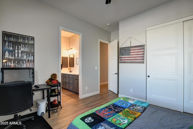 bedroom featuring baseboards, ensuite bath, wood finished floors, a sink, and a closet