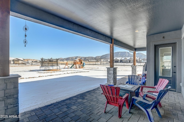 view of patio featuring a trampoline, a playground, a mountain view, and fence