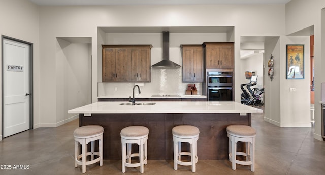 kitchen featuring black electric stovetop, wall chimney range hood, concrete flooring, stainless steel double oven, and a sink