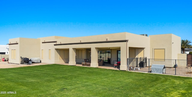 rear view of house featuring stucco siding, fence, a lawn, and a patio area