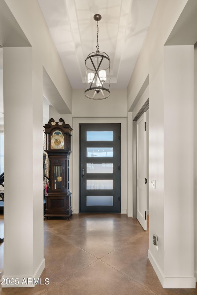 foyer featuring baseboards, concrete flooring, and an inviting chandelier