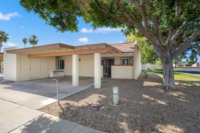 view of front of house with a tile roof, a carport, concrete driveway, stucco siding, and fence