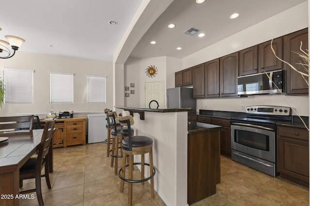 kitchen featuring a kitchen island, dark brown cabinetry, light tile patterned floors, and appliances with stainless steel finishes