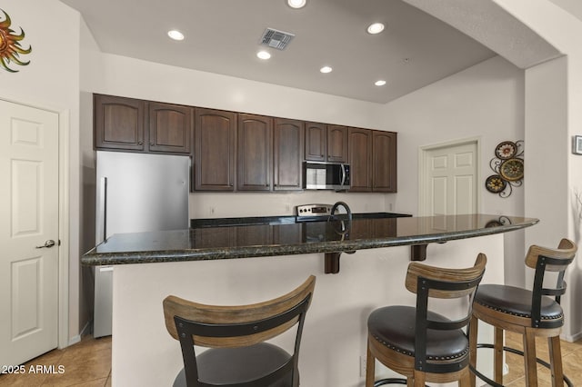 kitchen featuring stainless steel appliances, light tile patterned floors, a breakfast bar, a kitchen island, and dark brown cabinetry