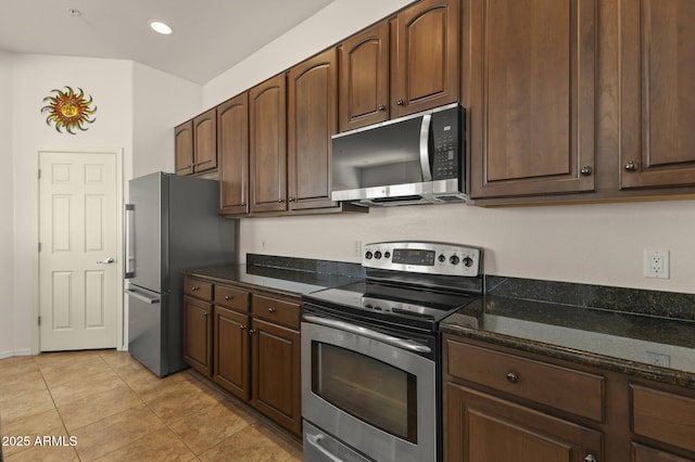 kitchen featuring light tile patterned floors, appliances with stainless steel finishes, dark brown cabinets, and dark stone counters