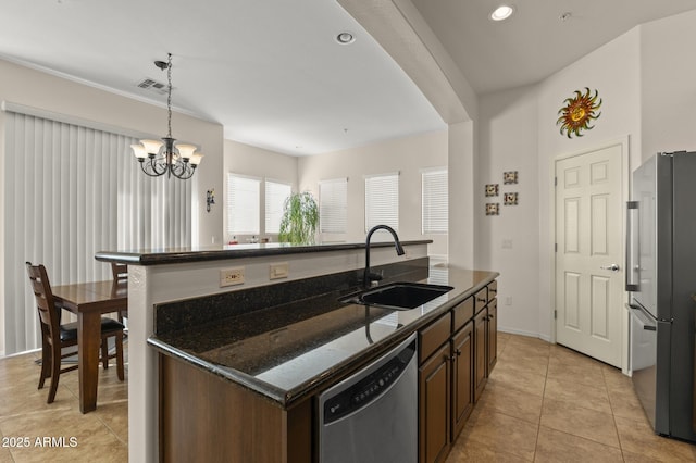 kitchen featuring pendant lighting, appliances with stainless steel finishes, dark stone counters, an island with sink, and sink